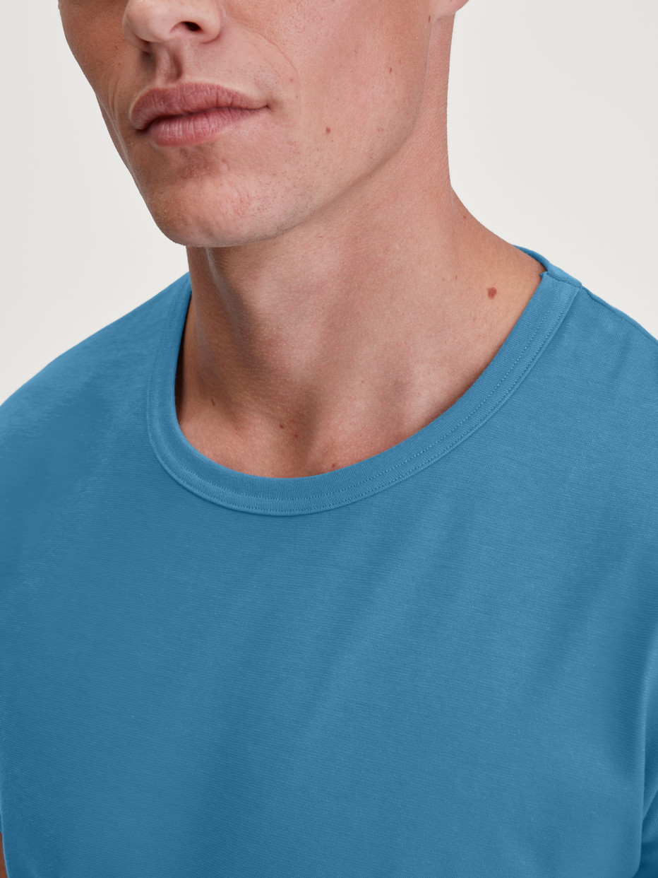 La modella / Il modello Uomo indossa Maglietta a maniche corte in 100% cotone di colore Blu, Tinta unita, della serie RMX Sleep Leisure di CALIDA, Dettaglio