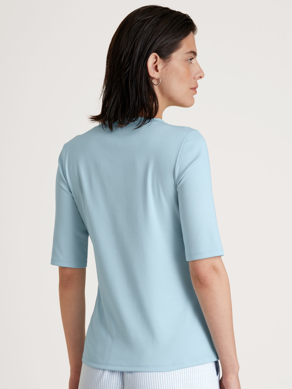 Damen-Model trägt Kurzarm-Shirt aus Baumwolle in Blau, Einfarbig aus Serie Amalfi Journey von CALIDA, Rückansicht