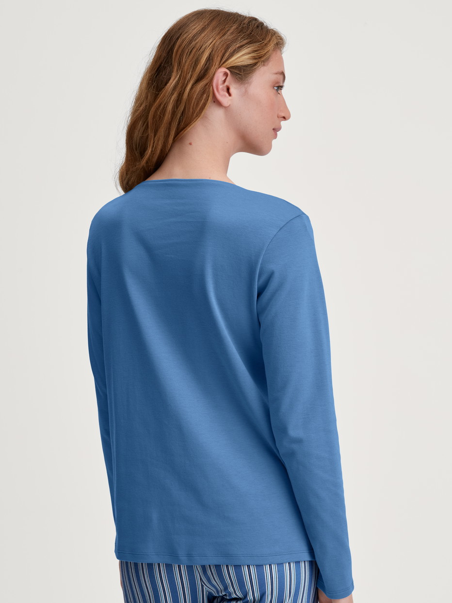 Damen-Model trägt Langarm-Shirt, V-Neck aus 100% Baumwolle in Blau, Einfarbig aus Serie Favourites Journey von CALIDA, Rückansicht