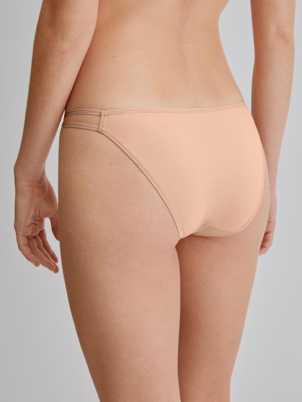 Women model is wearing Low Cut Tanga Brief made of Polyamide in Beige, Unicoloured from the Sleek Skin series by CALIDA, Back view