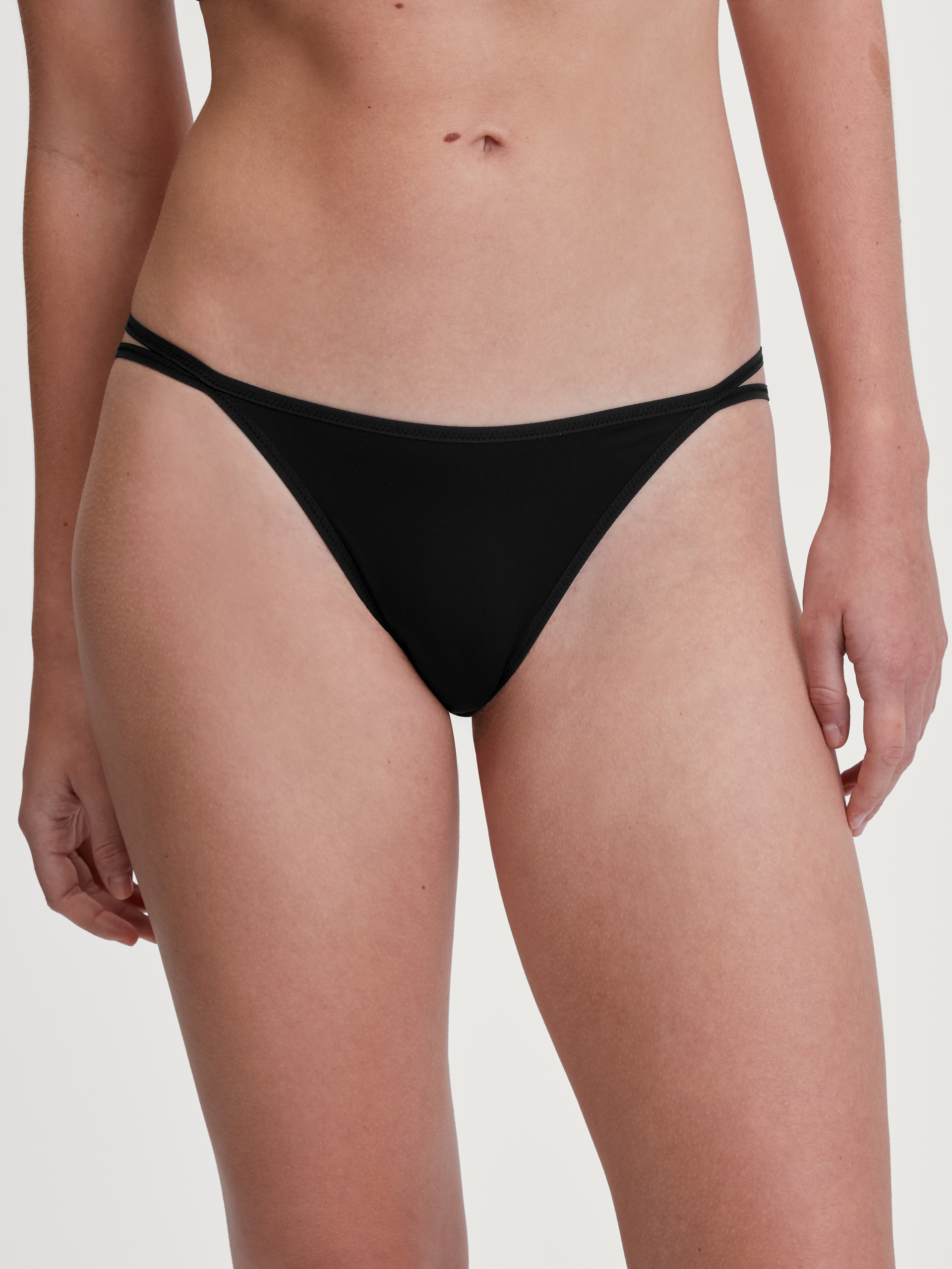 Women model is wearing Low Cut Tanga Brief made of Polyamide in Black, Unicoloured from the Sleek Skin series by CALIDA, Front view