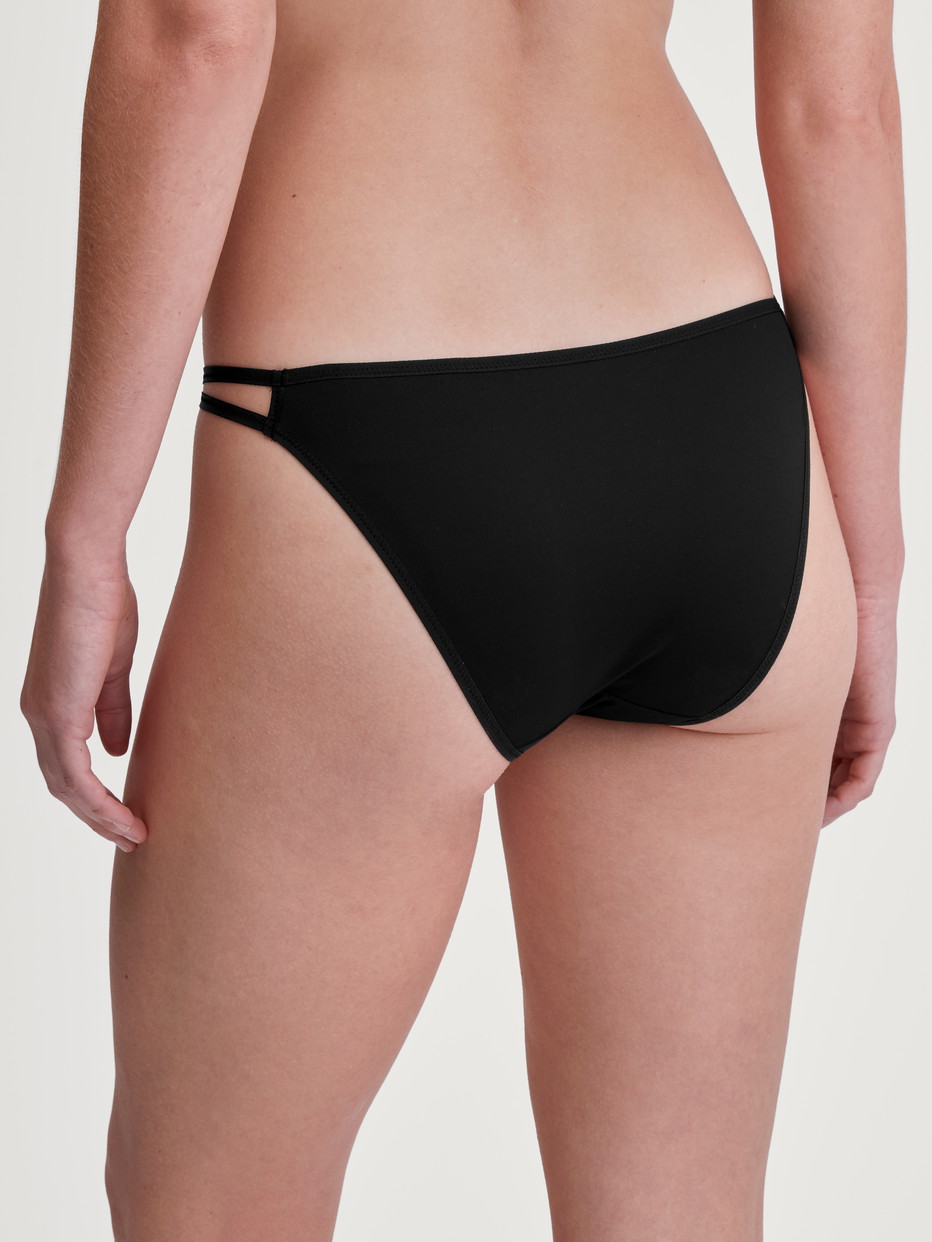 Damen-Model trägt Tanga-Slip, low cut aus Polyamid in Schwarz, Einfarbig aus Serie Sleek Skin von CALIDA, Rückansicht