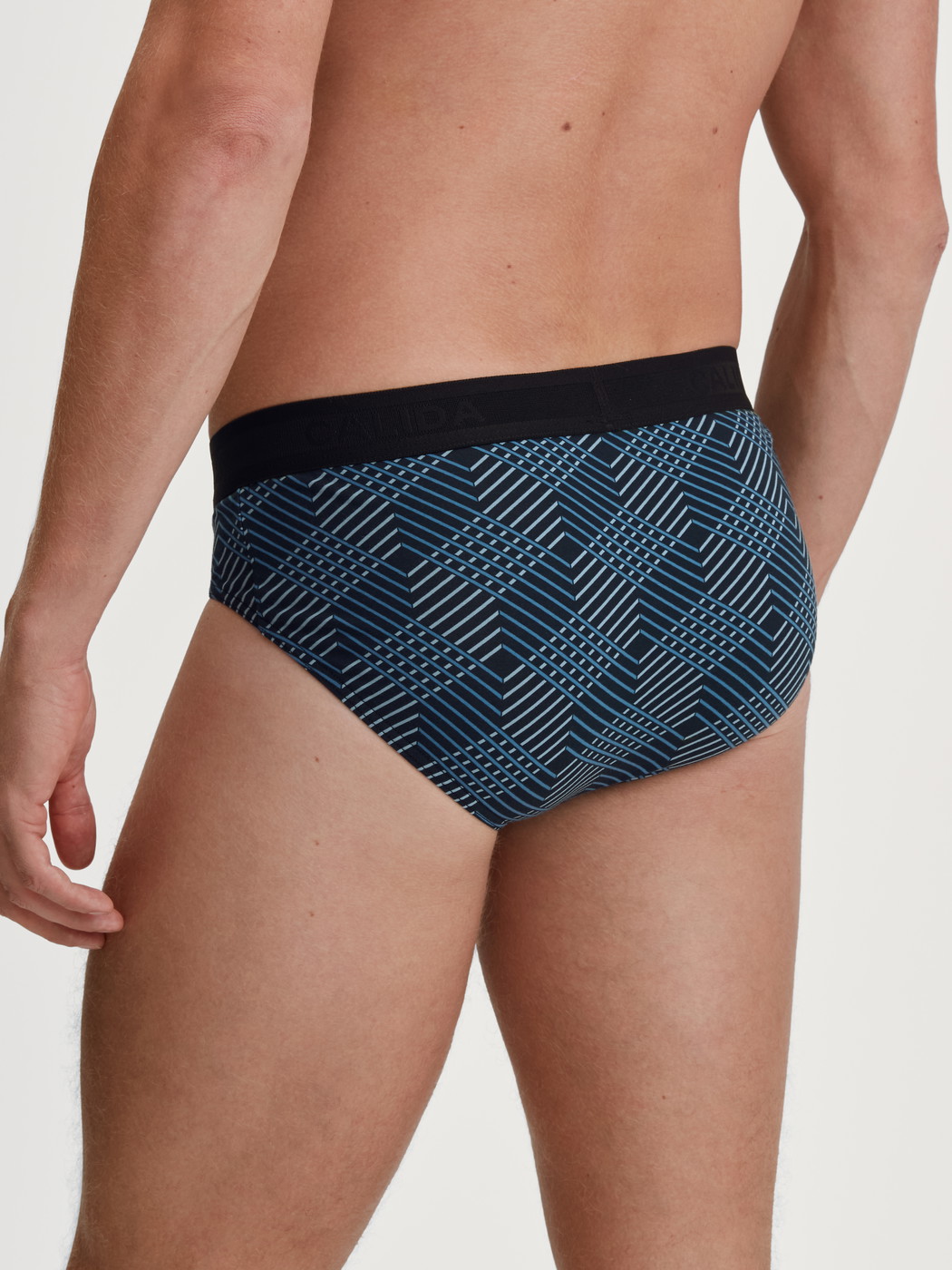 Herren-Model trägt Slip mit Softgummibund aus Baumwolle in Schwarz, Gemustert aus Serie Grafic Cotton von CALIDA, Rückansicht