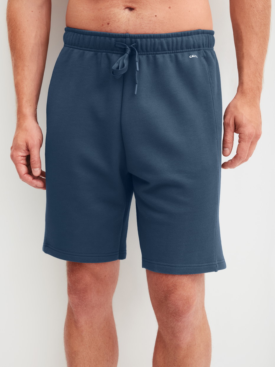 Herren-Model trägt Bermudas mit Seitentaschen aus Baumwolle in Blau, Einfarbig aus Serie RMX Lounge Journey von CALIDA, Vorderansicht