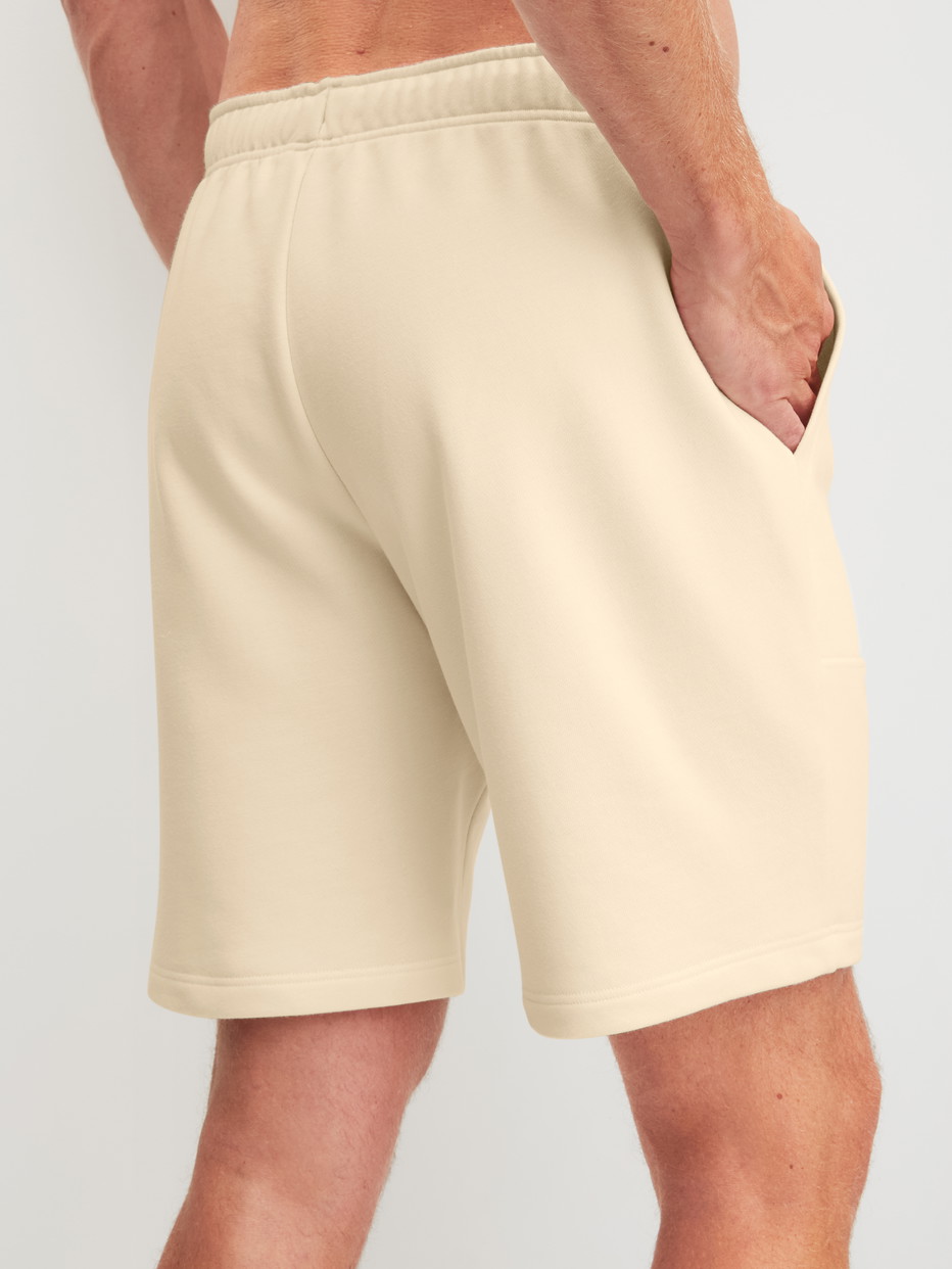 Herren-Model trägt Bermudas mit Seitentaschen aus Baumwolle in Beige, Einfarbig aus Serie RMX Lounge Lecce von CALIDA, Rückansicht
