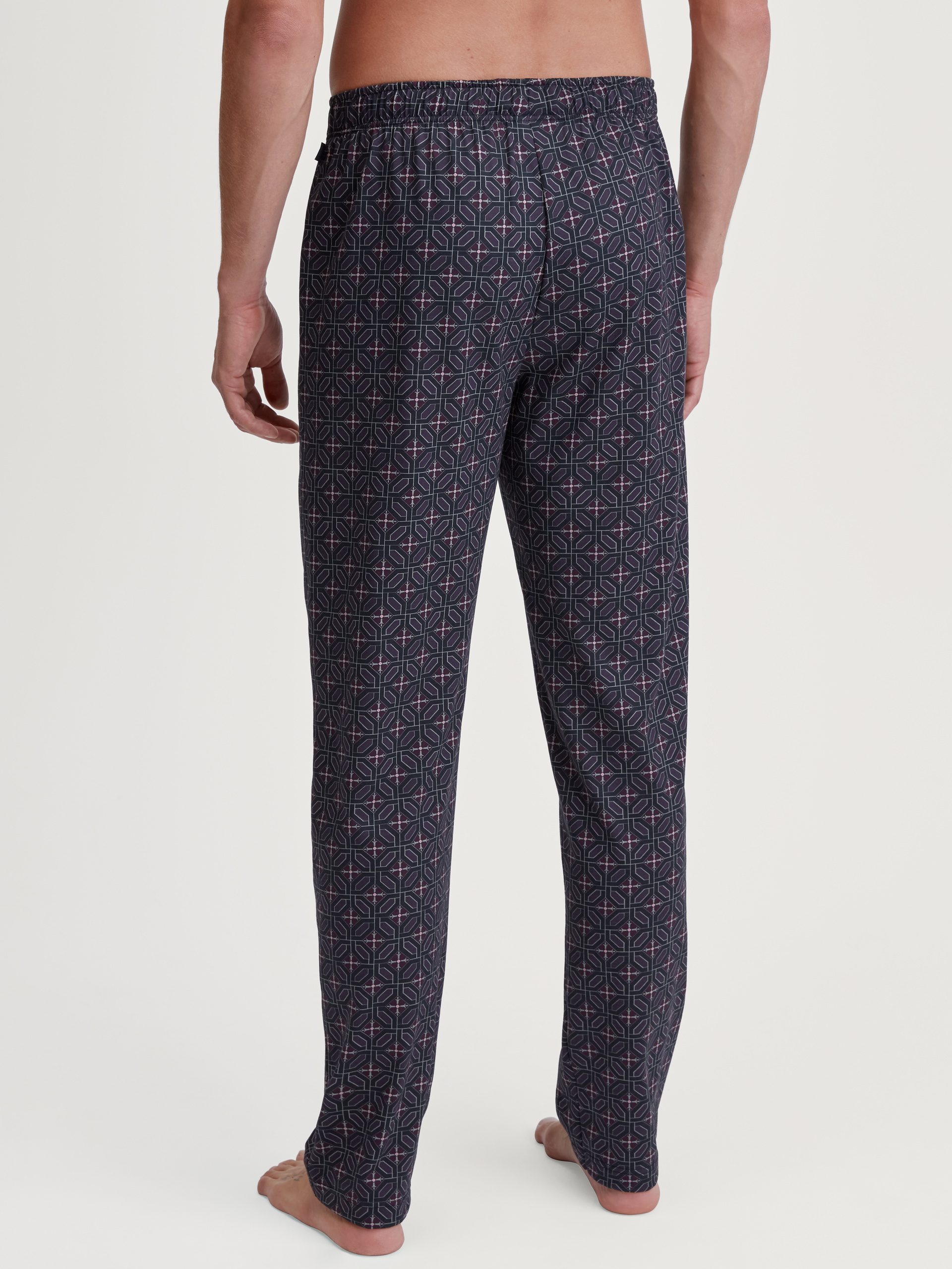 Herren-Model trägt Pyjamahose mit Seitentaschen aus 100% Baumwolle in Braun, Gemustert aus Serie RMX Sleep Holiday von CALIDA, Rückansicht