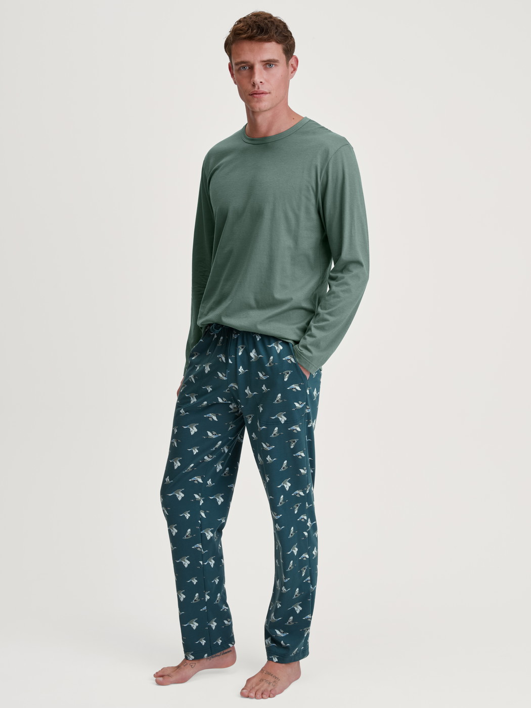Men model is wearing Pyjama Bottoms with Side Pockets made of 100% Cotton in Green, Patterned from the RMX Sleep Weekend series by CALIDA, Outfit