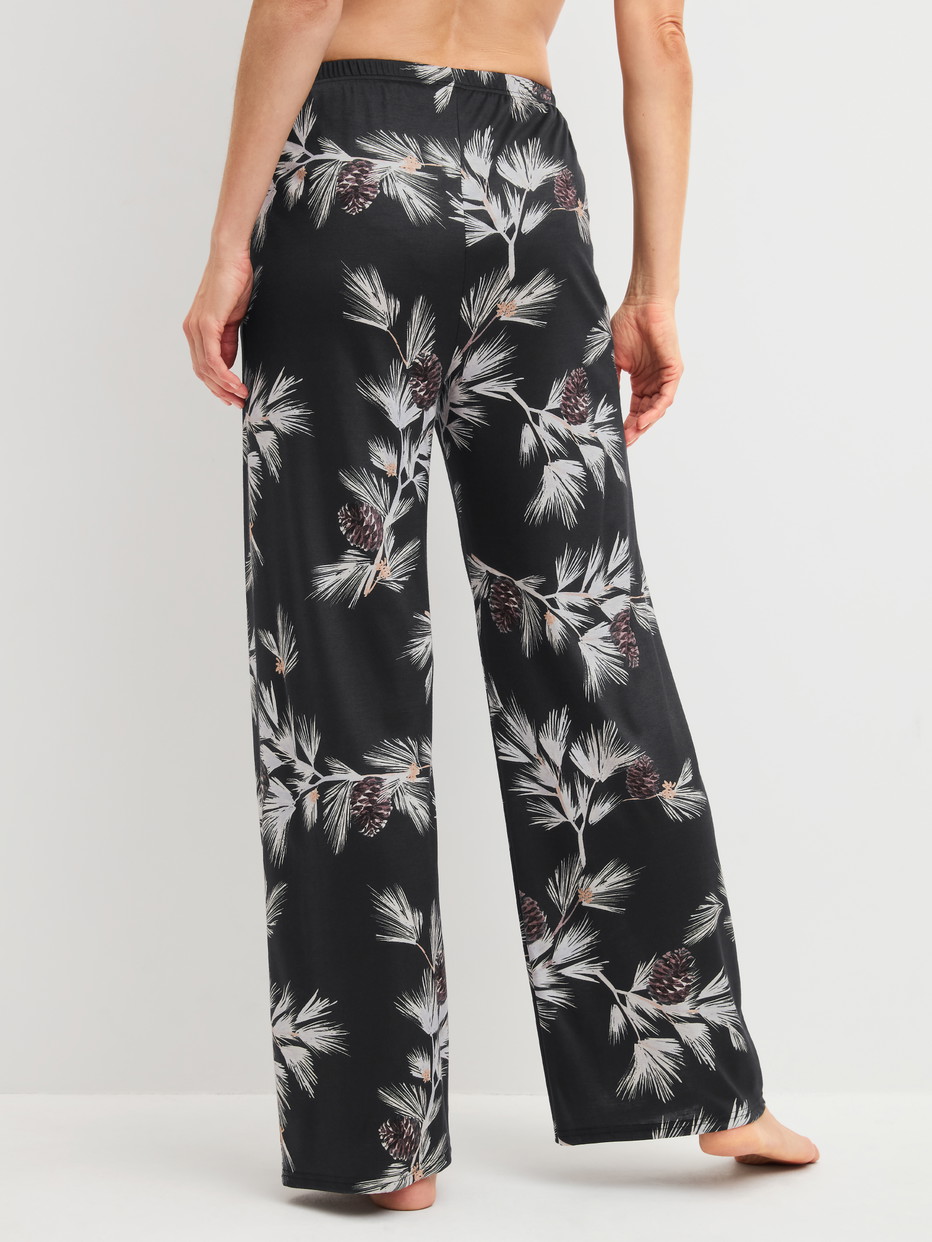Damen-Model trägt Pyjamahose mit Seitentaschen aus Modal in Schwarz, Floral aus Serie Glimmer M&M von CALIDA, Rückansicht
