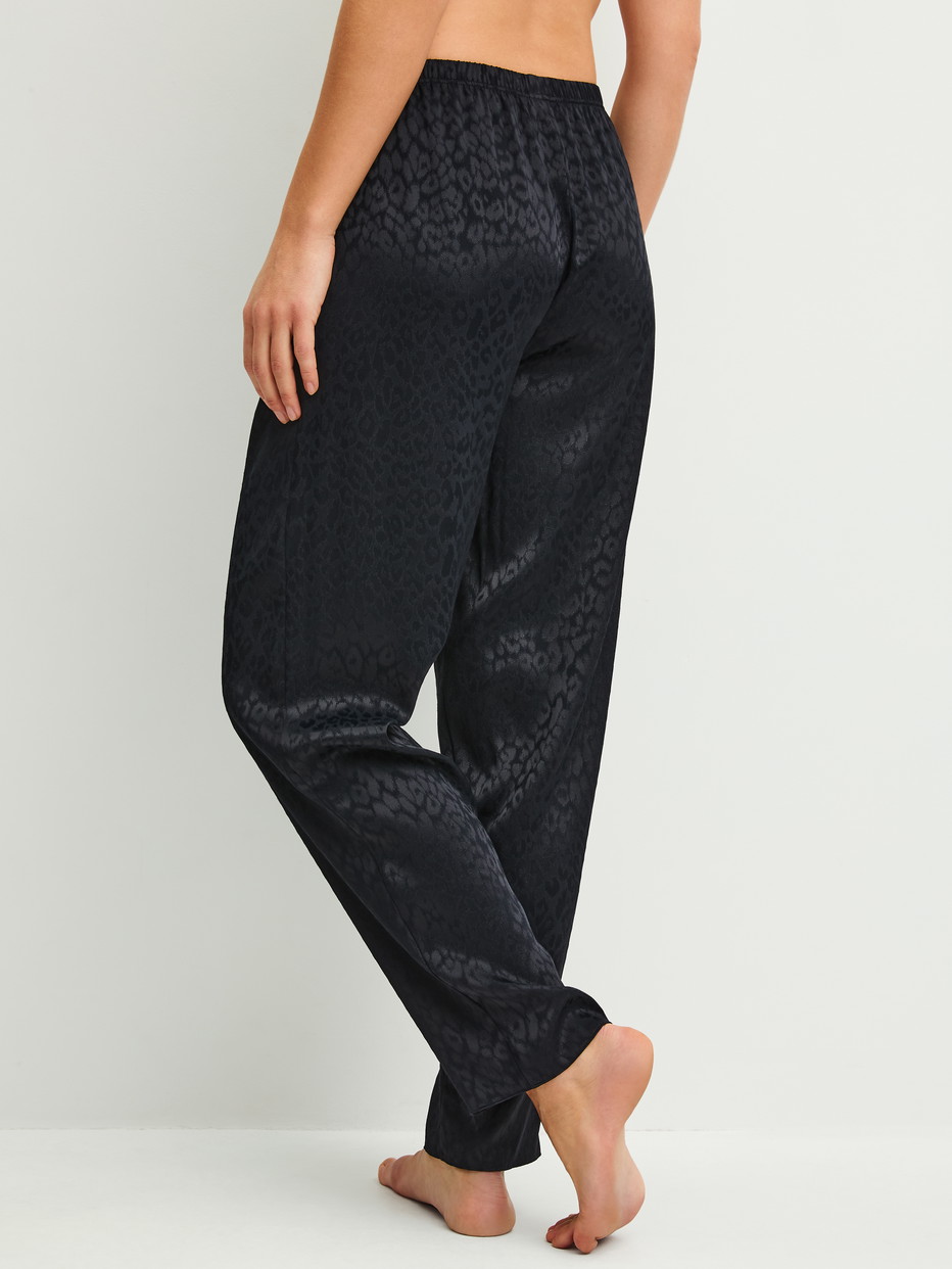 Damen-Model trägt Pyjamahose mit Seitentaschen aus Viskose in Schwarz, Gemustert aus Serie Glimmer M&M von CALIDA, Rückansicht