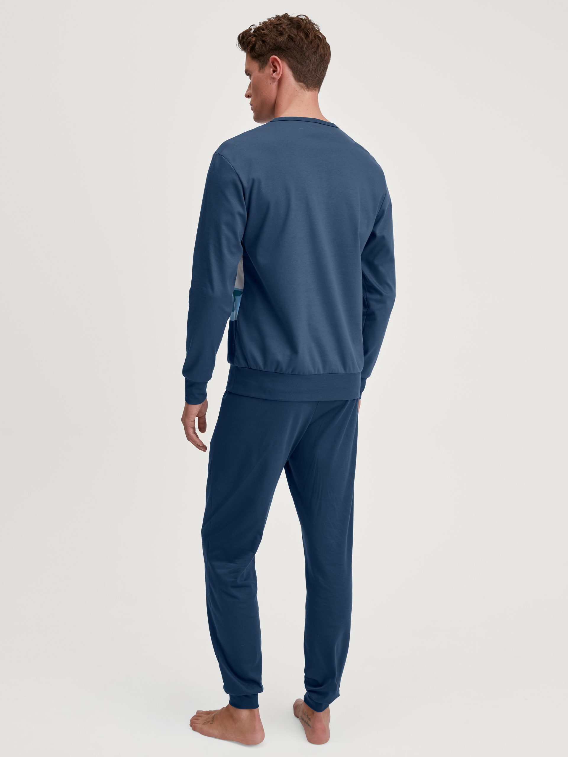Herren-Model trägt Bündchen-Pyjama aus 100% Baumwolle in Blau, Motiv aus Serie Relax Ski Resort von CALIDA, Rückansicht