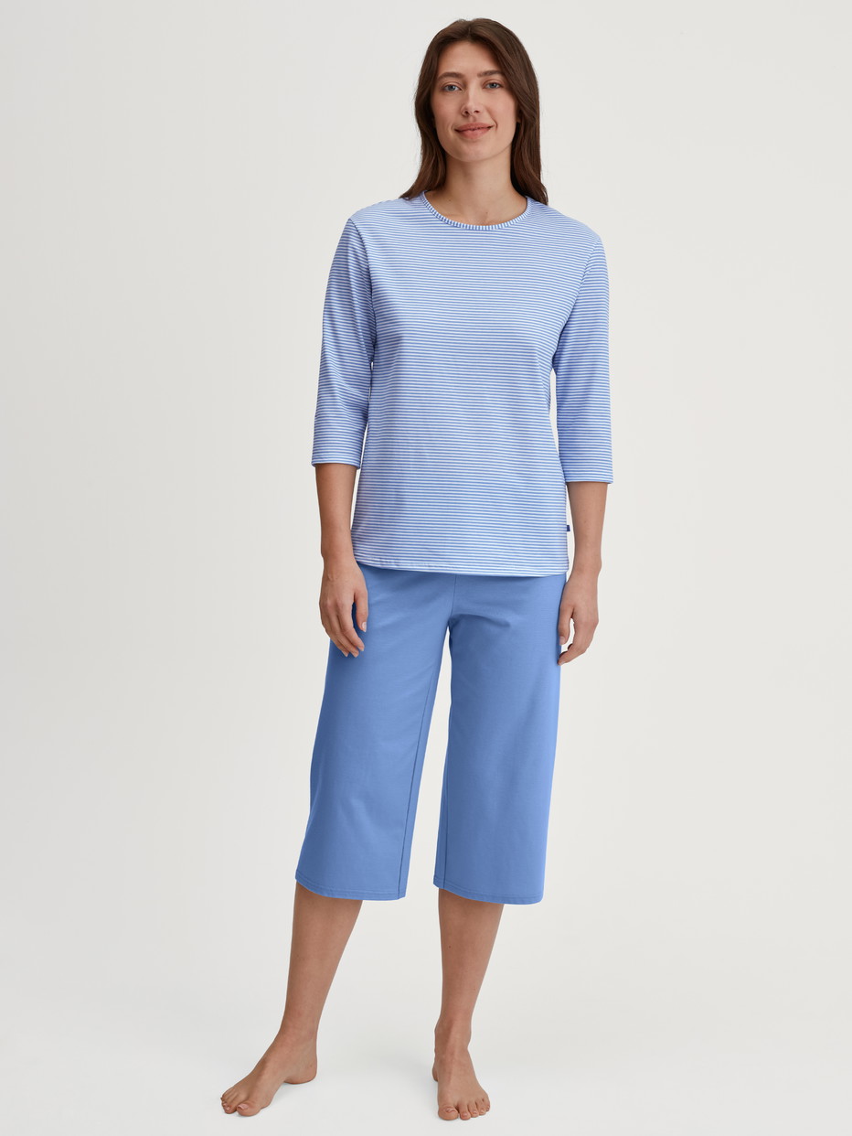 Women model is wearing Capri Pyjama made of 100% Cotton in Blue, Patterned from the Lovely Nights series by CALIDA, Front view