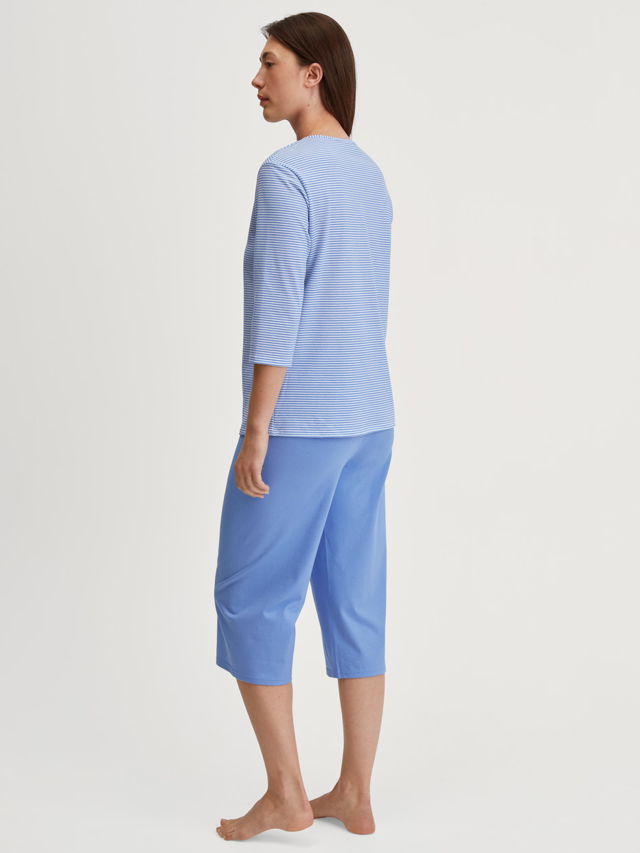 Women model is wearing Capri Pyjama made of 100% Cotton in Blue, Patterned from the Lovely Nights series by CALIDA, Back view