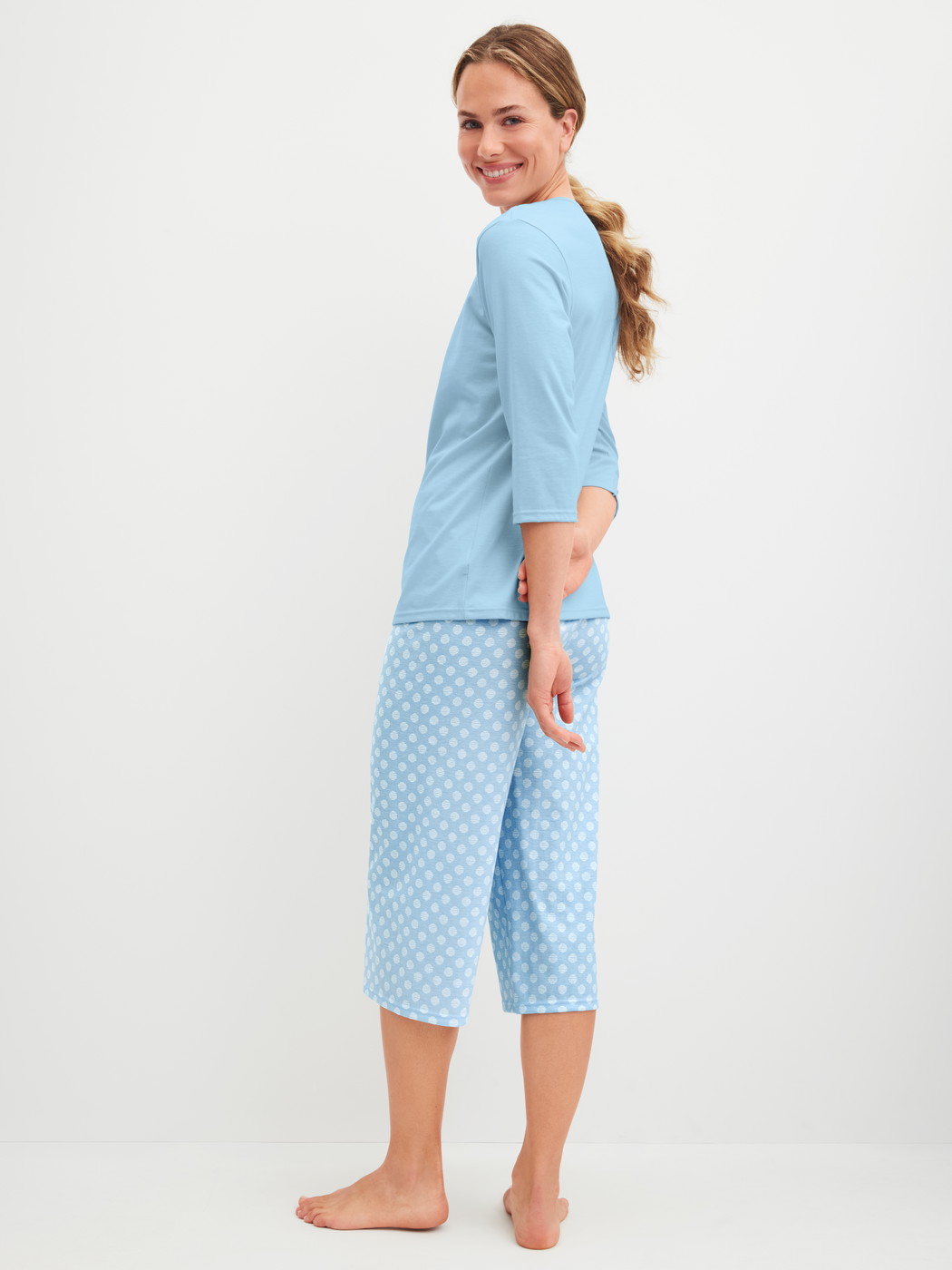 Women model is wearing Capri Pyjama made of 100% Cotton in Blue, Patterned from the Lovely Nights series by CALIDA, Back view